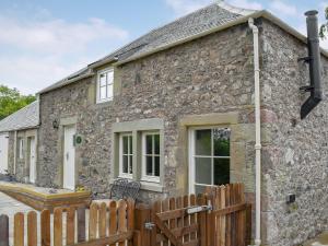 a stone cottage with a wooden fence in front of it at Grooms Bothy in Nenthorn