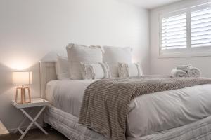 a white bedroom with a large bed with white pillows at Stay Coastal - Mission Bay in Auckland