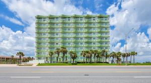 a large green building with palm trees in front of it at Galveston Luxury High Rise Oceanfront in Galveston