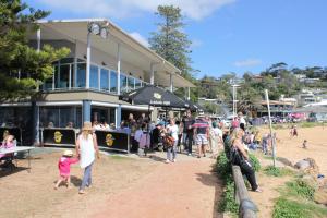 una folla di persone sulla spiaggia di fronte a un edificio di Avoca Beach "Cape Cottage" ad Avoca Beach