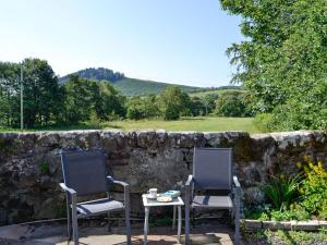 2 chaises et une table en face d'un mur en pierre dans l'établissement Belstane Cottage, à Straiton