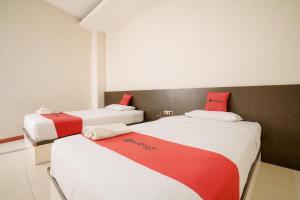 two beds in a room with red and white at RedDoorz near Pantai Pede in Labuan Bajo