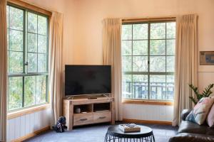 a living room with a flat screen tv and two windows at Country Lane Cottage in Halls Gap
