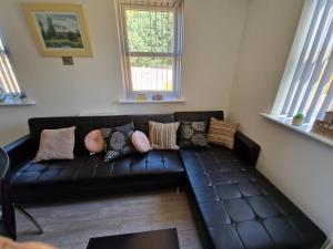 a black leather couch in a living room with windows at 7 Burnby Close,Leeds,LS14 1GA in Leeds