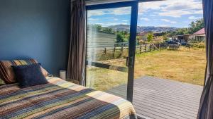 a bedroom with a bed and a large glass window at Rough Ridge Cottage ~ your haven in Central Otago in Oturehua