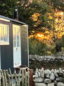 a small cabin with a fence and a stone wall at The Hazel Hut in Westport