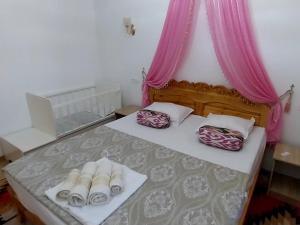Schlafzimmer mit einem Bett mit rosa Vorhängen und Hausschuhen in der Unterkunft NAZIRA Boutique Hotel in Xiva