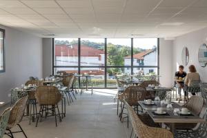 un restaurante con mesas, sillas y ventanas grandes en Nemea Appart Hotel Les Hauts de Milady Biarritz, en Biarritz