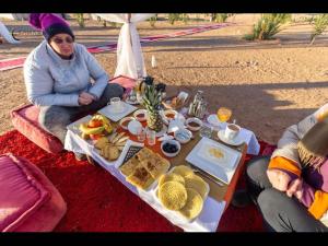 a woman sitting at a table with food on it at Over night at Merzouga Sahara Desert in Tisserdmine