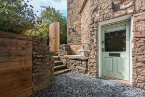eine grüne Tür in einem Steingebäude mit einem Zaun in der Unterkunft Eden's Peaceful Escape Apartment in Kendal