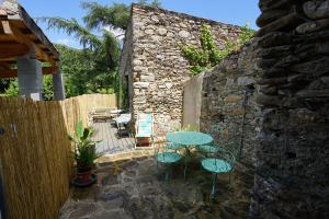 un patio con mesa y sillas junto a una pared de piedra en Les volets bleus en Prémian