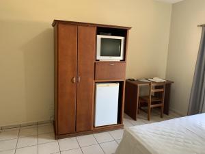 Ouro Hotel في أورينهوس: غرفة نوم مع تلفزيون وكابينة مع ثلاجة صغيرة