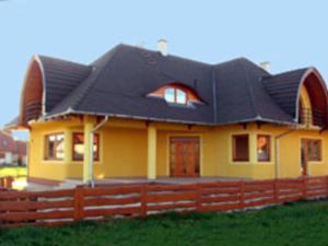 uma casa amarela com um telhado preto e uma cerca em Nádas Társasház em Balatonlelle