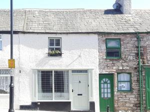 a stone house with a white door and green windows at Cobblers Cottage in Dalton in Furness