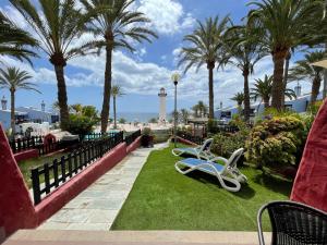 a lawn with palm trees and a bench and a lighthouse at Sun club playa del águila by la piedra viva in San Bartolomé de Tirajana
