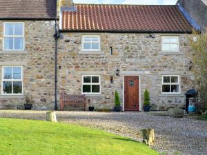 a stone house with a wooden door and a bench at Broats Barn in Ingleton