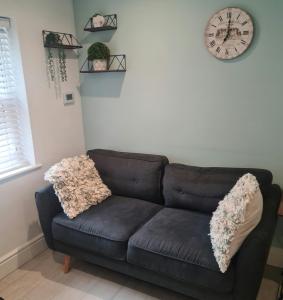 a black couch in a living room with a clock on the wall at 2 bed Home From Home Apartments in London