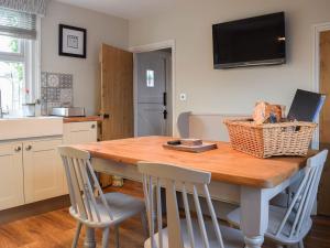 a kitchen with a wooden table with chairs and a television at Clickers Cottage in Woodford