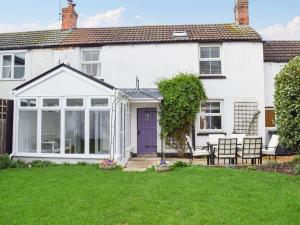 una casa blanca con una puerta púrpura y un patio en Clickers Cottage, en Woodford