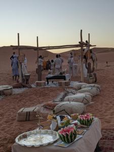 a group of people in the desert with a table with food at Sahara Majestic Luxury Camp in Merzouga