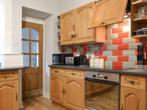 a kitchen with wooden cabinets and a tile wall at Firwood Apartment in Kilmun