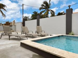 a swimming pool with chairs next to a white wall at Aruba Bliss Condos in Oranjestad