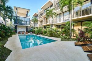 a swimming pool in front of a building with palm trees at Amena Condo Tulum in Tulum