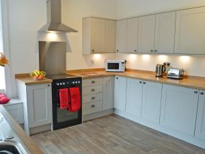 La cuisine est équipée de placards blancs et d'un four avec plaques de cuisson. dans l'établissement Halleaths Home Farm, à Lochmaben