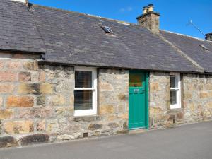 an old stone building with a green door and windows at Spey Cottage in Aberlour