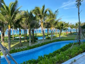 uma piscina com palmeiras e o oceano ao fundo em Seaview Arena Cam Ranh Nha Trang hotel near the airport em Cam Ranh