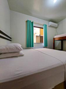 a bedroom with a large white bed with green curtains at Residencial Elpidio in Bombinhas