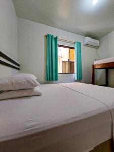 1 dormitorio con 1 cama blanca grande con cortinas verdes en Residencial Elpidio, en Bombinhas