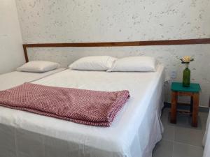 Una cama con dos almohadas y una mesa con un jarrón. en Casa de praia Prado Ba Doces magnólias, en Prado