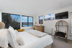 Dormitorio blanco con cama, silla y ventanas en Luxury Lake View Retreat with Hot Tub en Queenstown