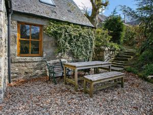 una mesa de picnic y un banco frente a una casa de campo en The Smiddy - S4278, en Lochearnhead