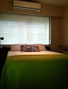 a bed with a green blanket and a window with a pillow at Studio Maipu in Buenos Aires