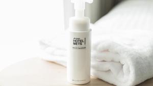 a white bottle of hair lotion next to a towel at JR-East Hotel Mets Koenji in Tokyo