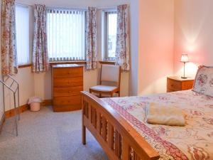 a bedroom with a bed and a chair and windows at Glen Apartment in Aviemore