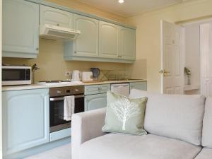 a kitchen with white cabinets and a couch with a pillow at Little Gables in Verwood