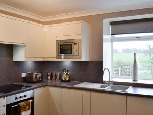 cocina con armarios blancos, fregadero y ventana en West Tannacrieff, en Stewarton
