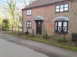 a brick house with a fence in front of it at Wilma Cottage in Geldeston