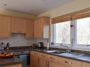 eine Küche mit Holzschränken, einem Waschbecken und 2 Fenstern in der Unterkunft Lochearnside Lodge in Saint Fillans