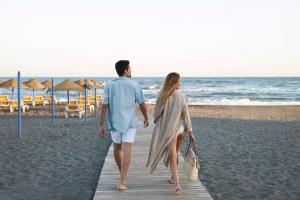 a man and woman walking down a wooden walkway on the beach at Iberostar Málaga Playa in Torrox Costa