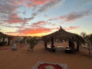 梅爾祖卡的住宿－Merzouga Camp & Desert Activities，沙漠中的小屋,背景是日落