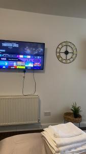 einen Flachbild-TV, der an einer Wand mit einer Uhr hängt in der Unterkunft Bv Comfy Studio At Deighton Huddersfield in Huddersfield