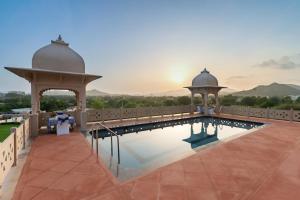 a swimming pool with a gazebo and a sunset at Traavista Aravali Mahal in Udaipur