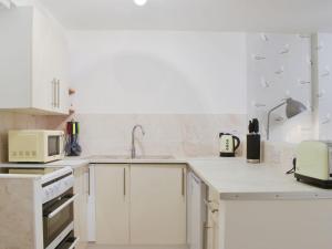 eine weiße Küche mit einer Spüle und einer Mikrowelle in der Unterkunft Millys Cottage in Ayton