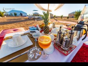 a table with a glass of orange juice on top of it at Merzouga Desert Luxury Camp in Tisserdmine