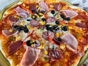 una pizza con jamón y aceitunas en un plato en Pensiunea DORA SASCA en Sasca Montană