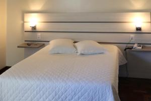 1 dormitorio con 1 cama blanca y 2 almohadas en Tri Hotel Xanxerê, en Xanxerê